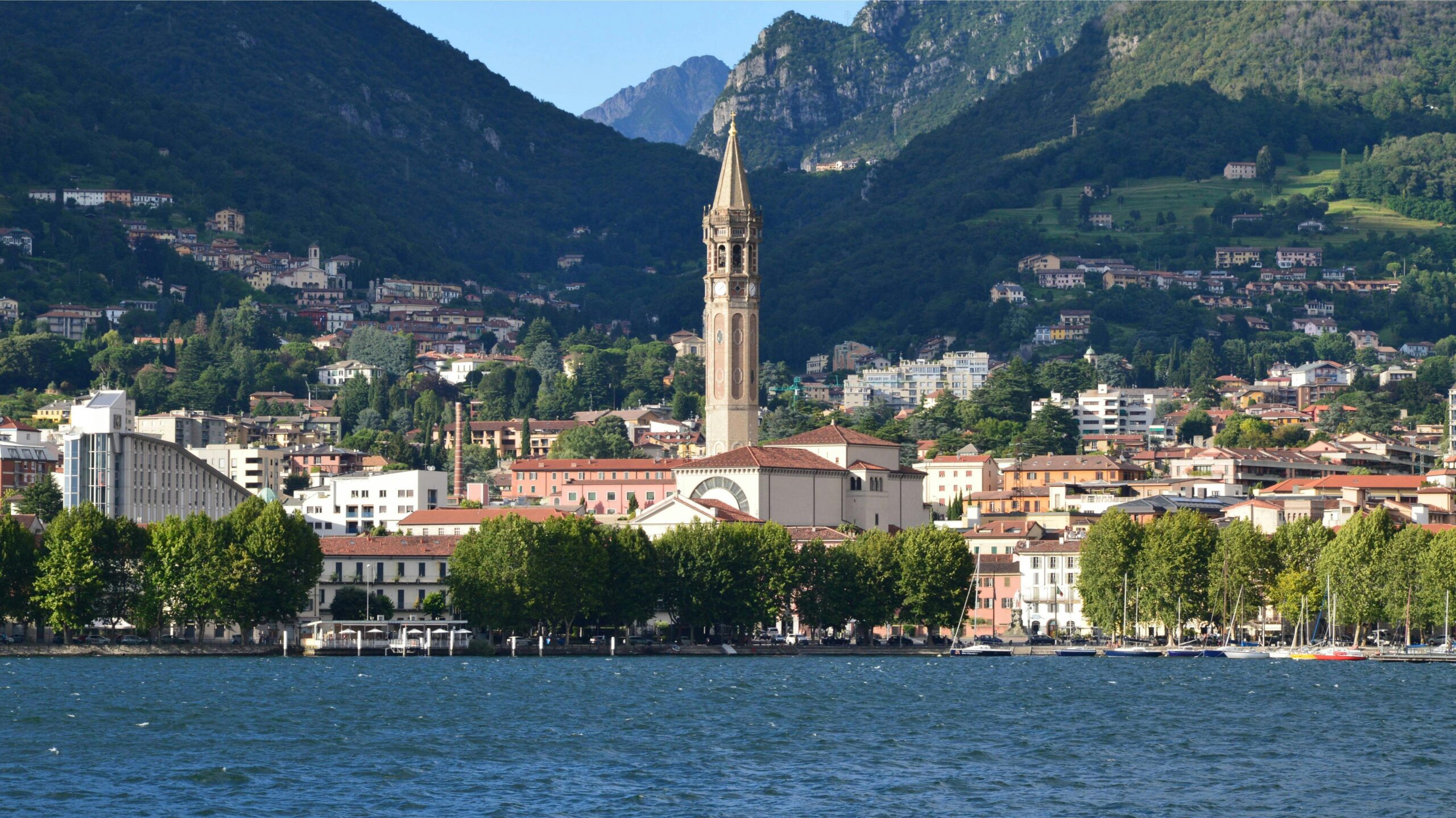 Picturesque view of Lecco with Basilica San Nicolo by the water, surrounded by lush mountains.